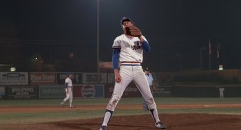 Movie still from “Bull Durham” (1988), directed by Ron Shelton – A baseball player holding a baseball glove on a baseball field at night; Wide shot, Low angle