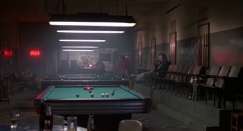 Movie still from “Bull Durham” (1988), directed by Ron Shelton – A group of people sitting around a pool table in a room; Wide shot, Over the shoulder angle