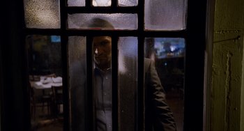 Movie still from “Bullet to the Head” (2012), directed by Walter Hill – A man standing behind a glass door looking out; Medium shot, Over the shoulder angle