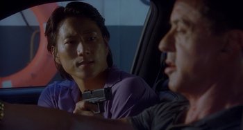Movie still from “Bullet to the Head” (2012), directed by Walter Hill – A man and a woman sitting in a car holding a gun; Close Up shot, Over the shoulder angle