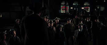 Movie still from “Butch Cassidy and the Sundance Kid” (1969), directed by George Roy Hill – A group of men in hats and jackets standing in a dark room; Wide shot, Over the shoulder angle