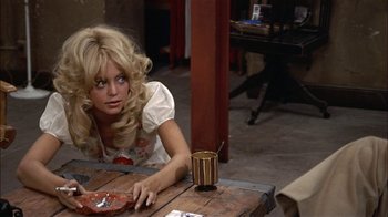 Movie still from “Butterflies Are Free” (1972), directed by Milton Katselas – A woman sitting at a wooden table with a cup of coffee; Medium shot, High angle