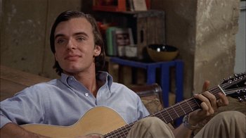 Movie still from “Butterflies Are Free” (1972), directed by Milton Katselas – A man sitting on the ground holding a guitar; Close Up shot, High angle