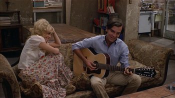 Movie still from “Butterflies Are Free” (1972), directed by Milton Katselas – A man playing a guitar while sitting on a couch next to a woman; Medium shot, High angle