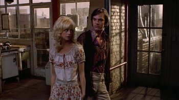Movie still from “Butterflies Are Free” (1972), directed by Milton Katselas – A man and a woman standing next to each other in front of a brick building; Medium shot, Over the shoulder angle