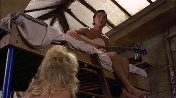 Movie still from “Butterflies Are Free” (1972), directed by Milton Katselas – A shirtless man sitting on top of a wooden structure; Medium shot, Overhead angle