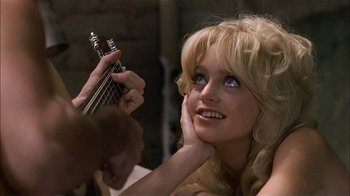 Movie still from “Butterflies Are Free” (1972), directed by Milton Katselas – A woman holding a guitar in front of a brick wall; Close Up shot, Over the shoulder angle