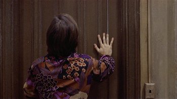 Movie still from “Butterflies Are Free” (1972), directed by Milton Katselas – A woman in a purple and orange shirt reaching her hand up to the side of a wall; Medium shot, High angle