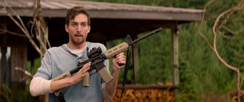 Movie still from “Cabin Fever” (2016), directed by Travis Zariwny – A man holding an ar - 1 5 style rifle in his hands; Medium shot, Over the shoulder angle