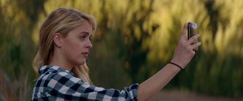 Movie still from “Cabin Fever” (2016), directed by Travis Zariwny – A woman holding a cell phone up to the side of her face; Close Up shot, Over the shoulder angle