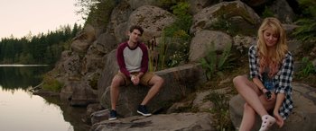 Movie still from “Cabin Fever” (2016), directed by Travis Zariwny – A young man sitting on a rock in the woods; Wide shot, High angle