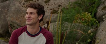 Movie still from “Cabin Fever” (2016), directed by Travis Zariwny – A young man smiles while standing in front of some plants; Close Up shot, Over the shoulder angle