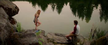 Movie still from “Cabin Fever” (2016), directed by Travis Zariwny – Two people sitting on rocks near a body of water; Wide shot, High angle
