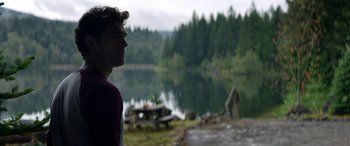 Movie still from “Cabin Fever” (2016), directed by Travis Zariwny – A man standing in front of a body of water; Medium shot, Over the shoulder angle
