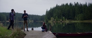 Movie still from “Cabin Fever” (2016), directed by Travis Zariwny – A woman sitting on a dock next to a boat; Wide shot, Low angle
