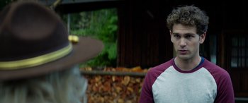 Movie still from “Cabin Fever” (2016), directed by Travis Zariwny – A young man standing in front of a pile of wood; Close Up shot, Over the shoulder angle