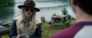 Movie still from “Cabin Fever” (2016), directed by Travis Zariwny – A woman wearing a hat and sunglasses in front of a lake; Close Up shot, Over the shoulder angle