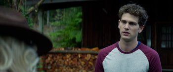 Movie still from “Cabin Fever” (2016), directed by Travis Zariwny – A young man standing in front of a pile of wood; Close Up shot, Over the shoulder angle