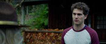 Movie still from “Cabin Fever” (2016), directed by Travis Zariwny – A young man standing in front of a pile of wood; Close Up shot, Over the shoulder angle