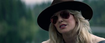 Movie still from “Cabin Fever” (2016), directed by Travis Zariwny – A woman wearing sunglasses and a hat with trees in the background; Close Up shot, Over the shoulder angle