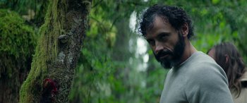 Movie still from “Cabin Fever” (2016), directed by Travis Zariwny – A bearded man standing next to a tree in the woods; Close Up shot, Over the shoulder angle