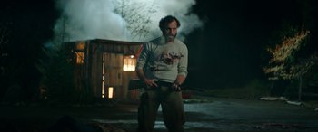Movie still from “Cabin Fever” (2016), directed by Travis Zariwny – A man holding a gun while standing in front of a building; Medium shot, Over the shoulder angle