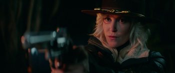 Movie still from “Cabin Fever” (2016), directed by Travis Zariwny – A woman in a hat holding a gun in a dark room; Close Up shot, Over the shoulder angle