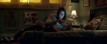 Movie still from “Cabin Fever” (2016), directed by Travis Zariwny – A woman is sitting on a bed looking at a tablet; Medium shot, High angle