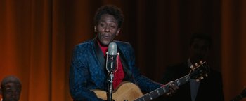 A man sitting in front of a microphone holding a guitar
