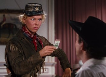 Movie still from “Calamity Jane” (1953), directed by David Butler – A woman in a cowboy hat holding up a dollar bill to a man; Medium shot, Over the shoulder angle