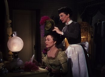 Movie still from “Calamity Jane” (1953), directed by David Butler – Two women in old - fashioned clothing are standing in front of a lamp; Medium shot, Low angle