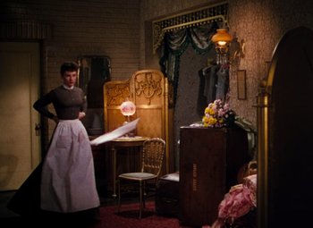 Movie still from “Calamity Jane” (1953), directed by David Butler – A woman standing in front of a chair in a living room; Wide shot, High angle