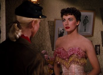 Movie still from “Calamity Jane” (1953), directed by David Butler – A woman in a pink and yellow dress looking at another woman in a military uniform; Medium shot, Over the shoulder angle