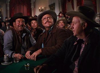 Movie still from “Calamity Jane” (1953), directed by David Butler – A group of men sitting at a table in a room; Medium shot, Low angle