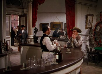 Movie still from “Calamity Jane” (1953), directed by David Butler – Two men sitting at a bar in front of a wine glass; Wide shot, High angle