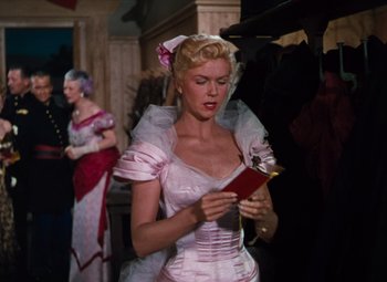 Movie still from “Calamity Jane” (1953), directed by David Butler – A woman in a pink dress looking at a red book; Medium shot, Over the shoulder angle