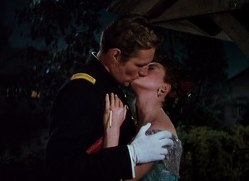 Movie still from “Calamity Jane” (1953), directed by David Butler – A man and a woman kissing each other in formal wear; Medium shot, Low angle