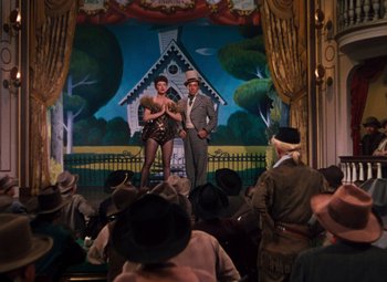 Movie still from “Calamity Jane” (1953), directed by David Butler – A man and a woman are standing on a stage in front of an audience; Wide shot, Low angle