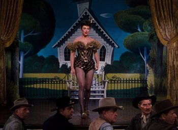 Movie still from “Calamity Jane” (1953), directed by David Butler – A woman is standing in front of a painting of a house; Wide shot, Low angle
