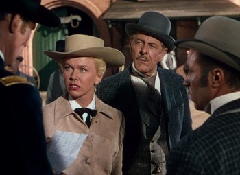 Movie still from “Calamity Jane” (1953), directed by David Butler – A group of people standing next to each other wearing hats; Medium shot, Over the shoulder angle