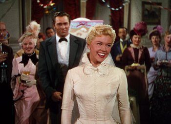 Movie still from “Calamity Jane” (1953), directed by David Butler – A woman in a white dress standing in front of a group of people; Medium shot, Low angle