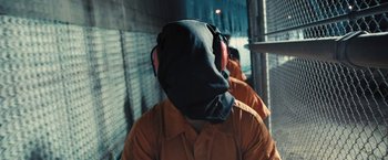 Movie still from “Camp X-Ray” (2014), directed by Peter Sattler – A man with headphones on his head in an orange suit; Medium shot, Over the shoulder angle