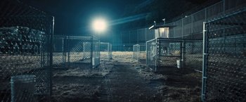 Movie still from “Camp X-Ray” (2014), directed by Peter Sattler – A fenced in area at night with a light shining; Extreme Wide shot, High angle