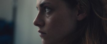 Movie still from “Camp X-Ray” (2014), directed by Peter Sattler – A woman's face in a dark room; Extreme Close Up shot, Over the shoulder angle