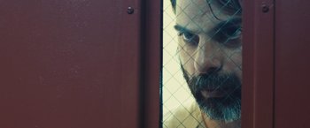 Movie still from “Camp X-Ray” (2014), directed by Peter Sattler – A man with a goatee looking through a fence; Close Up shot, Over the shoulder angle