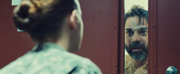 Movie still from “Camp X-Ray” (2014), directed by Peter Sattler – A woman looking in the mirror of a red door; Close Up shot, Over the shoulder angle
