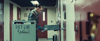 Movie still from “Camp X-Ray” (2014), directed by Peter Sattler – A woman in a military uniform holding a book; Medium shot, Over the shoulder angle