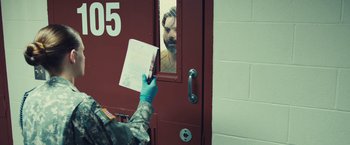 Movie still from “Camp X-Ray” (2014), directed by Peter Sattler – A person holding a pen in front of a door; Medium shot, Over the shoulder angle