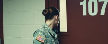 Movie still from “Camp X-Ray” (2014), directed by Peter Sattler – A woman in a military uniform looking out of a window; Medium shot, Over the shoulder angle