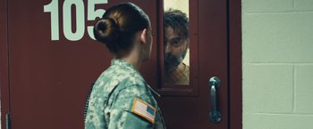 Movie still from “Camp X-Ray” (2014), directed by Peter Sattler – A man and a woman are looking at each other through a window; Medium shot, Over the shoulder angle